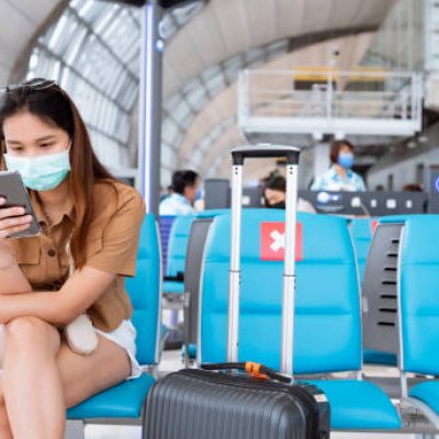 Asian woman wearing a mask sits in the terminal at the airport. New normal in air travel.